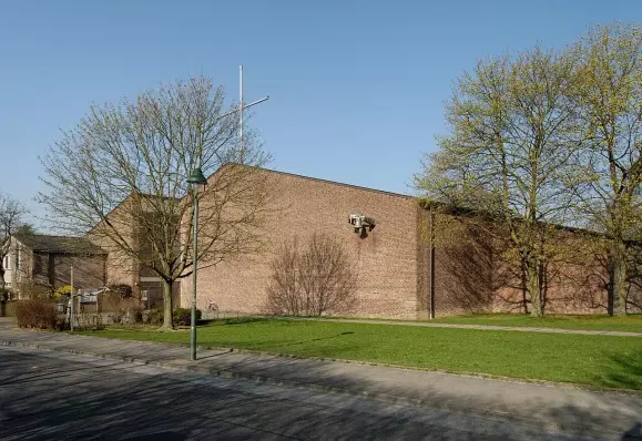 The image shows a brick building set against a clear blue sky. There are trees nearby, some of which are just starting to bud, indicating it might be spring. There is also a grassy area in front of the building, with a sidewalk. The overall scene appears to be quite serene and well-maintained.

Image Credits: Wikimedia / Wiegels / CC BY 3.0