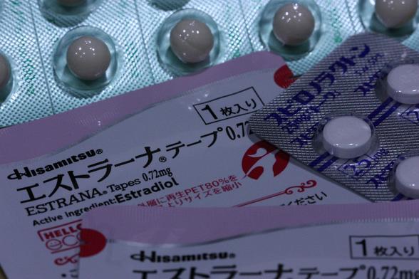 A macro shot featuring packets of medication: estradiol patches, spironolactone tablets and progesterone capsules