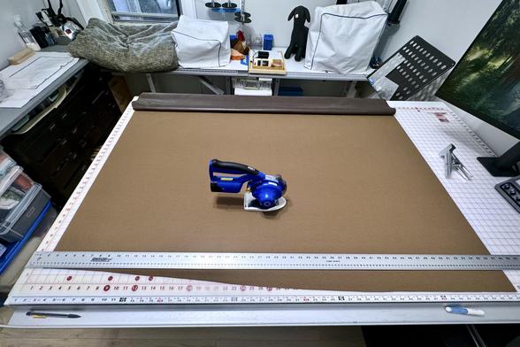 Chocolate brown fleece-backed vinyl on a large cutting table with the wrong-side up getting squared up. There is a cordless fabric cutter in the centre.
