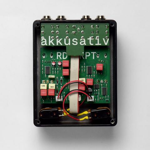 Photo. Top down view of the insides of the pedal. Two green circuit boards connected with a ribbon cable. IO board has "akkusativ" written on it, main board has "RDRPT" on it.

Components are mostly SMD except an ungodly amount of THD caps of all shapes and colors.