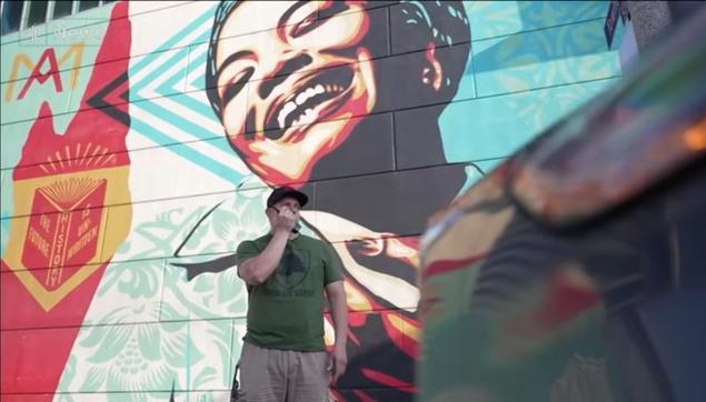 teaser picture for the YouTube link:

a man in a green shirt is standing in front of a painted wall using a walki-talki