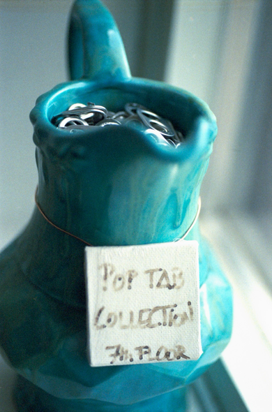 A turquoise pitcher, filled with soda can tabs, sits on a windowsill.