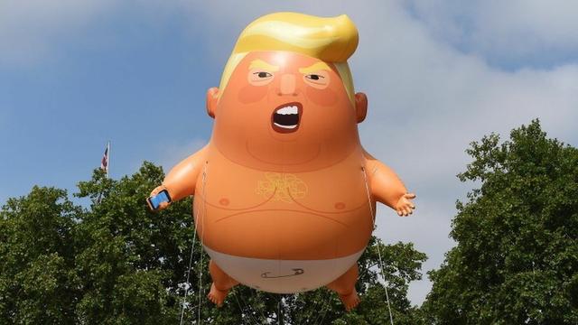 A giant balloon in the shape of a Trump Man-Baby. He is holding a cell phone, wearing a diaper, and crying like a baby.