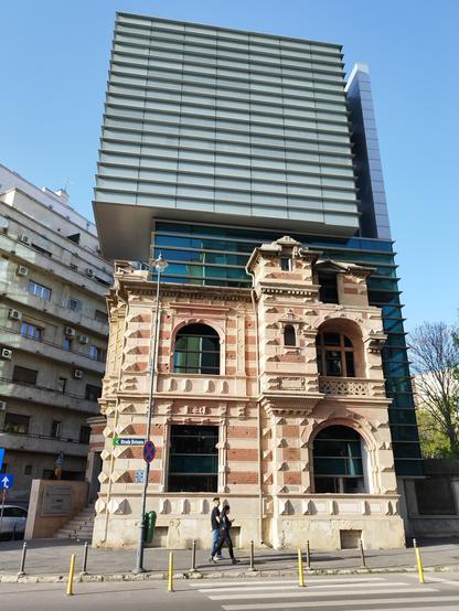 Auf ein historisches Gebäude wurde ein moderner Aufbau draufgesetz. Im Hintergrund ein weiteres Haus aus grauem Beton wie es oft in Bukarest zu sehen ist.