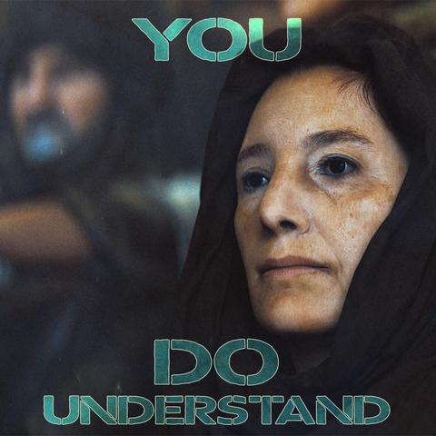 Portrait of a woman with a headscarf, while an out of focus man with a headscarf and beard is behind her to the left.  "You DO Understand" is written on top.