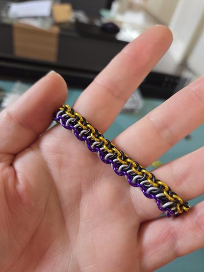 A vipera berrus bracelet in matt grey, matt white, gloss yellow, and gloss purple, held stretched out in my hand
