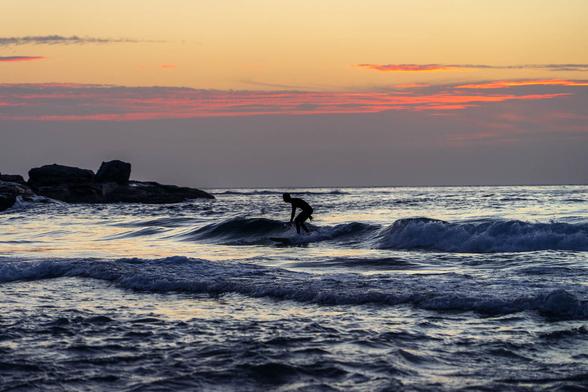 A lone surfer rides a small wave near the shore of Wollongong City Beach under the soft golden light of early morning.