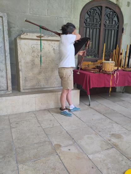 A person in modern dress playing a single drone set of bagpipes.