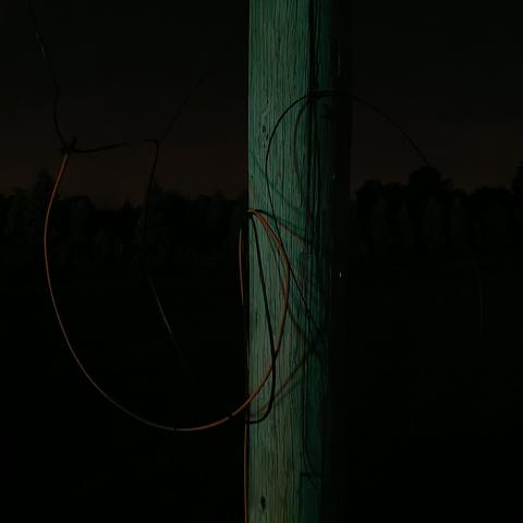 fallen and frayed orange and black wires from a wooden pole, lit green and bluish with an orange sky behind