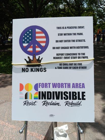 Sign on a trifold that reads:

This is a peaceful event.

Stay within the park.

Do not enter the streets.

Do not engage with agitators.

Report concerns to the nearest event staff or FWPD.

Be chill but be fire and take care of each other!

Fort Worth Area Indivisible.

Resist. Reclaim. Rebuild.