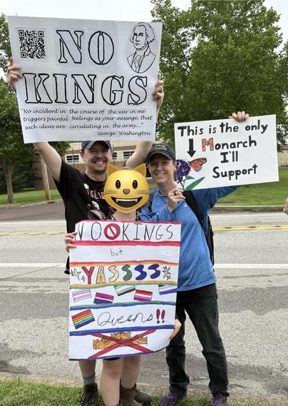 Two individuals are holding colorful protest signs. One sign states "NO KINGS" with a quote from George Washington. The other sign reads, "This is the only Monarch I'll Support," accompanied by a drawing of a butterfly.