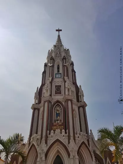 The image depicts a tall church tower featuring a cross at the top. The architecture appears intricate, with ornate designs and a prominent clock. There are also palm trees visible in the foreground, suggesting a warm climate. The sky is partly cloudy, adding to the atmospheric feel of the scene.

Image Credits: Wikimedia / Ashish Murugan / CC BY-SA 4.0