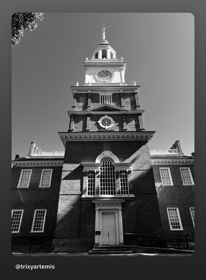 Black and white photo of Independence Hall in Philadelphia, showing the brick façade, tall windows, and the iconic clock tower rising above the building.