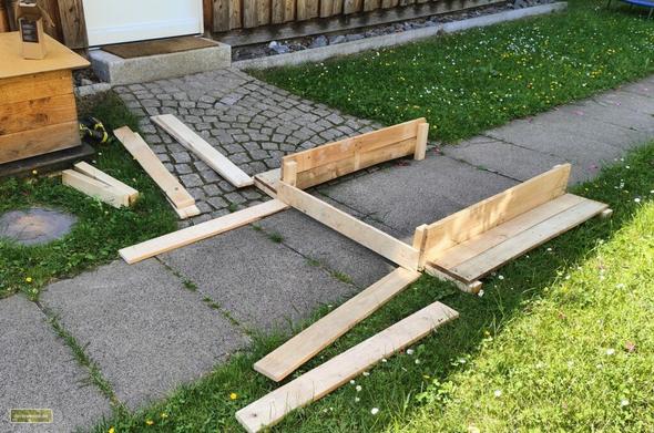 ein Dutzend Bretter, die auf einem Gehweg liegen und gerade zu einem Kastenbeetrahmen montiert werden.
