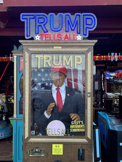 A photo of a seaside fortune telling machine, with a Trump automaton dressed in full Trump regalia, ready to tell you your fortune when you insert a coin.