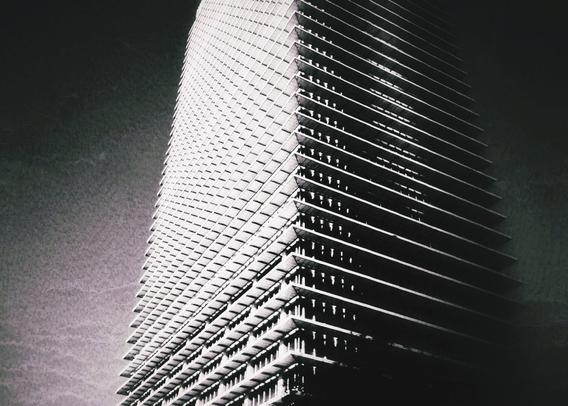 A black and white photo showing a low angle view of a tall apartment tower.