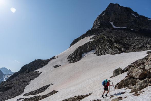A person is crossing a snowfield in the bottom right of the photo. Behind rises a rocky mountain peak
