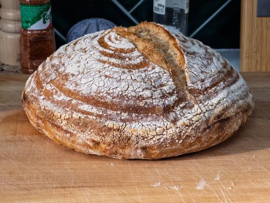 A freshly baked round loaf of crusty bread on a wooden cutting board.