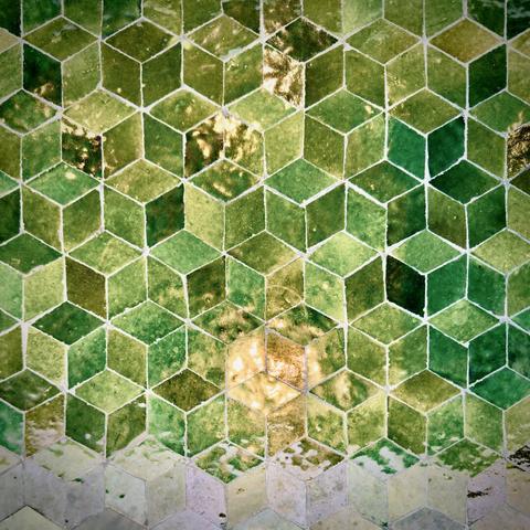 An outdoor tabletop comprised of many green diamonds forming isometric cubes reflects an incandescent lightbulb from above for the top seven-eighths of the image and a cloudy sky for the bottom eighth, creating what looks like a green beach shoreline in the process.