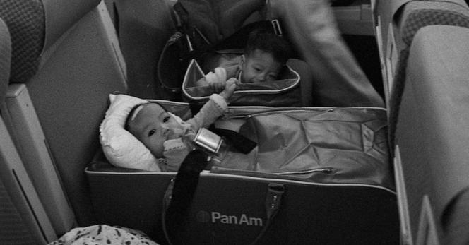 A black and white photo of a baby in a crib on an airplane.
