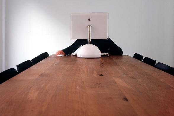 Leerer, langer Tisch an dessen Kopfende ein klassischer Apple Computer steht, dahinter eine Person.