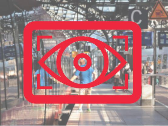 Ein Überwachungs-Auge, im Hintergrund ein Bahnhof