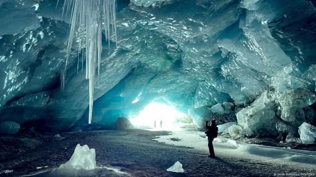 A woman takes a picture in one of the ice caves formed by water during the summer on the tongue the Morteratsch glacier