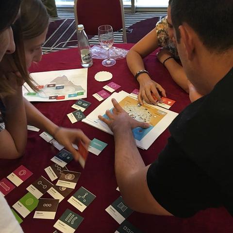 A group of people gathered around a table, interacting with tiles and printed pages.