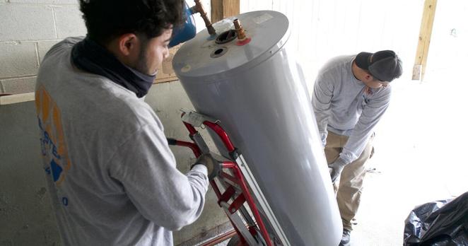 Angel Gomez (L) and Franes Mendez, technicians at heating, cooling and plumbing company John G. Webster, remove a gas water heater from a home in Washington, DC, on August 28, 2024. Heat pumps are an energy-efficient system for replacing both a heater and air conditioner in one appliance. Heat pump hot water heaters also exist. Hoping to spur heat pump uptake, the Inflation Reduction Act, President Joe Biden's 2022 landmark climate bill, provides up to $2,000 in tax credits for those installing either type. (Photo by Bastien INZAURRALDE / AFP) (Photo by BASTIEN INZAURRALDE/AFP via Getty Images)