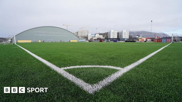 A low view of an artificial pitch, taken from one corner, looking towards high rise flats and a mountain in the distance