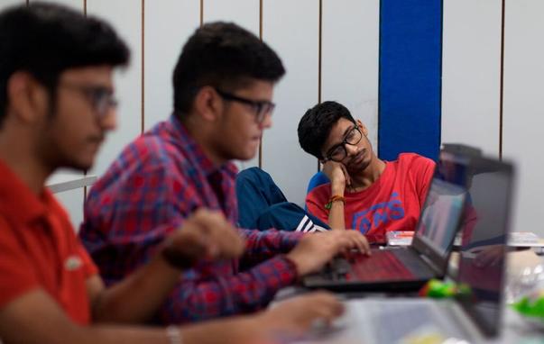 Image of two people typing at computers, with a third in the back dozing off with his head resting on his hand.