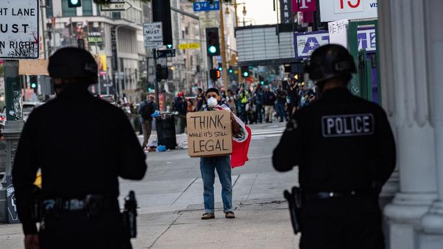 Man holding Think While It's Still Legal sign in front of police