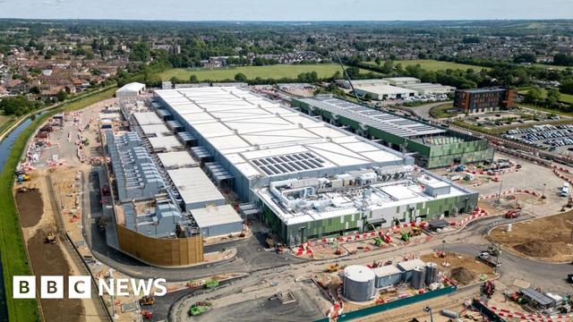 A large white data centre building under construction in Hertfordshire, surrounded by green land, a river and housing estates further afield.