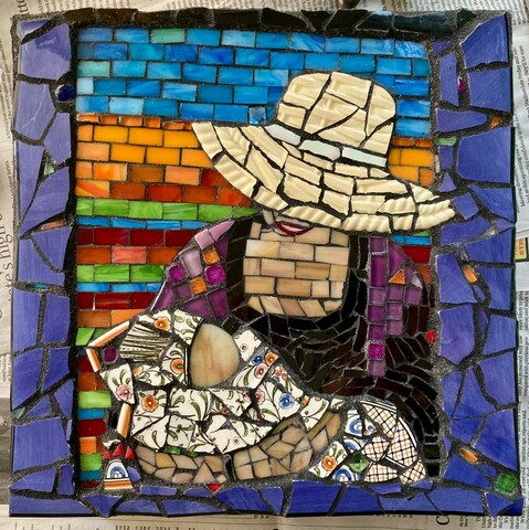 This mosaic is affixed to a 12”x12” cement garden paver.  The grout is dark gray.  A baby wrapped in an orange, blue, and green floral and checked blanket is held by a grandmother wearing a large, floppy, cream-colored, straw hat.  The smiling grandmother gazes down at the sleeping baby.  The colorful background is horizontal stripes of orange, blue, green, and red tiles (based on the upholstery at a favorite Mexican restaurant).  The piece is bordered in deep purple pieces from a recycled broken platter—to resemble looking through a window frame.