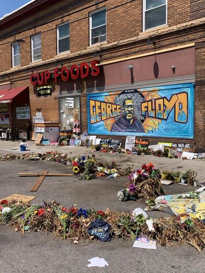 Side of building with iconic George Floyd mural. Memorials on street including a wooden cross. 2020