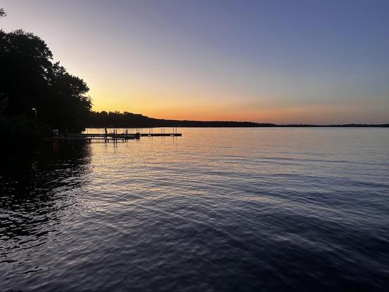 Calm lake sunset. A person walks on a dock