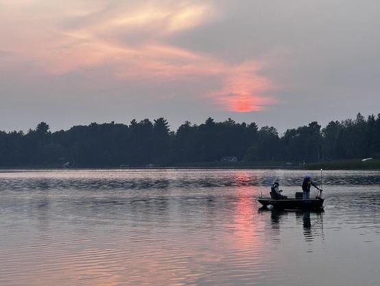 Cloudy sunset on a lake; a couple of young people fishing in a small boat.