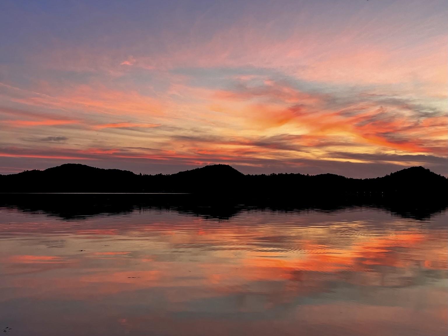 A serene sunset over a calm lake, with vibrant hues of orange, pink, and purple reflecting on the water's surface. Silhouetted hills frame the scene, enhancing the peaceful atmosphere. A serene sunset over a calm lake, with vibrant hues of orange, pink, and purple reflecting on the water's surface. Silhouetted hills frame the scene, enhancing the peaceful atmosphere.