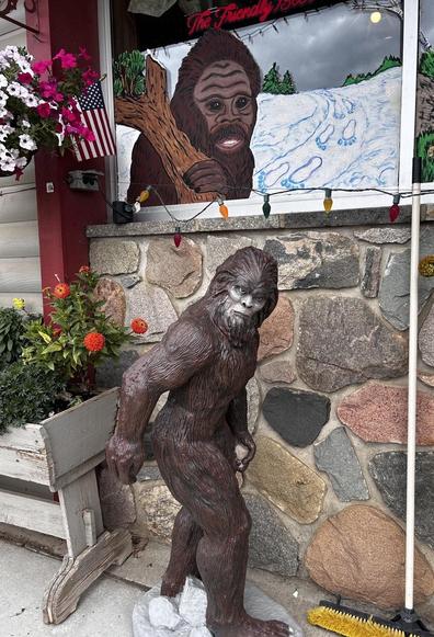 Statue of a hairy creature in front of a storefront that also includes a mural of such a creature showing tracks in the snow