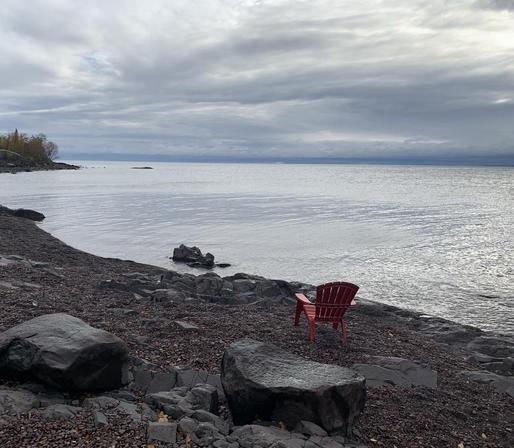 Calm lake scene with low clouds. The back of an empty red chair