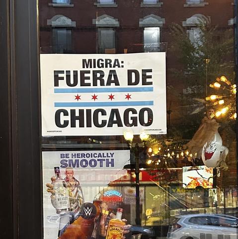 A sign 
MIGRA: FUERA DE CHICAGO 
with horizontal blue lines and 4 red stars 
