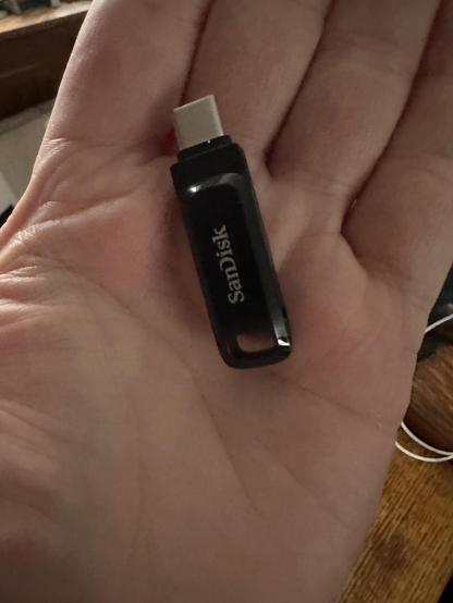 A light skinned hand holds a small black device with SanDisk printed on it.