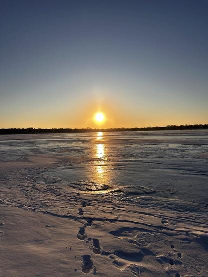 Setting sun approaching the horizon over a frozen lake.