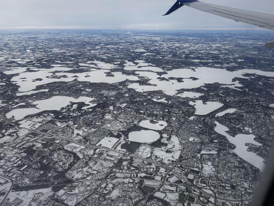 A flat, snow covered suburban landscape (towns, roads) with a number of ice covered lakes. One of them is elongated, with many bays, and is so large it doesn't fit in the photo frame.