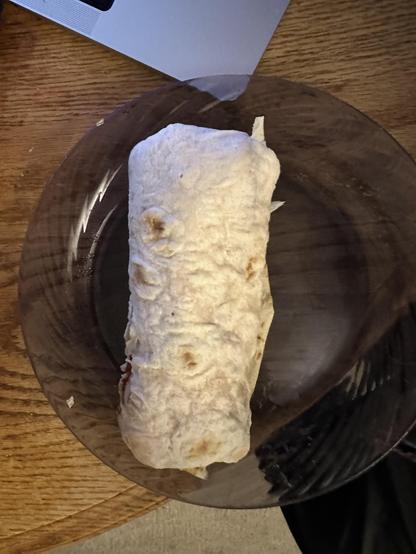 A beige cylinder sits on a deep purple clear plate. It looks like a burrito.
