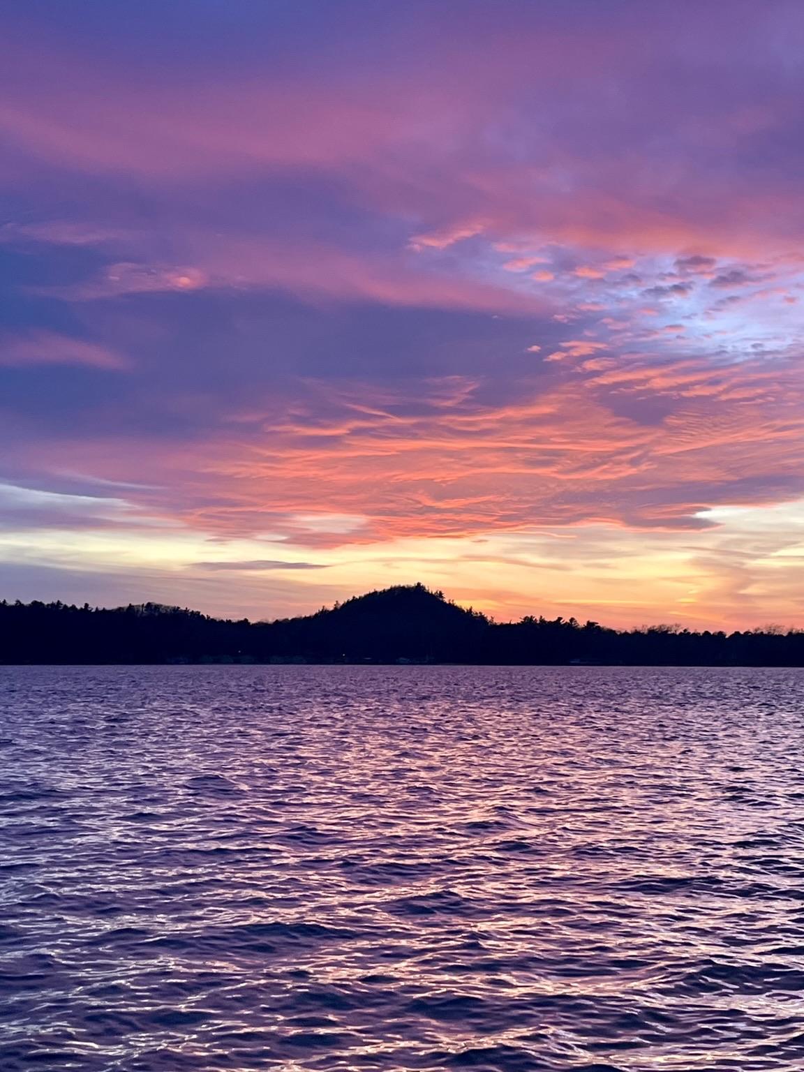 A sunset over a choppy lake. The sunset is orange at the horizon and lights the bottom of a large undulating cloud with bright red. Above this the clouds are a purplish color. The choppy water does not provide a symmetrical view, but instead resolves to a diffuse purplish color. Some nights the water is purple and this was one of those special nights.