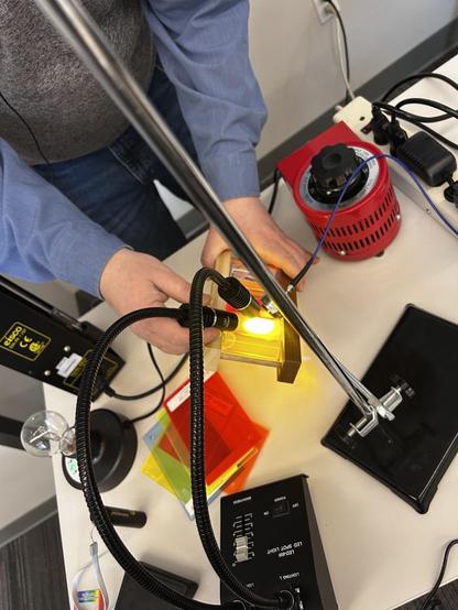 A person hold a vial of yellow liquid under a UV source, while simultaneously holding a detector.