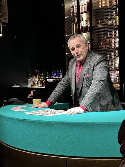 A man behind a desk covered in green felt. A deck of cards is spread out.