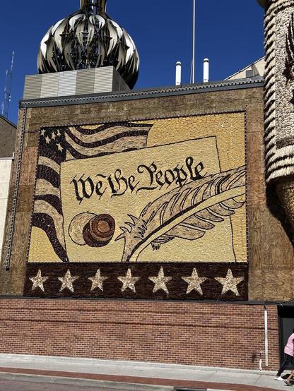 Closer view of one of the mosaics. A waving US flag with a document in front  saying We The People, a quill pen, and ink well, and seven stars.
