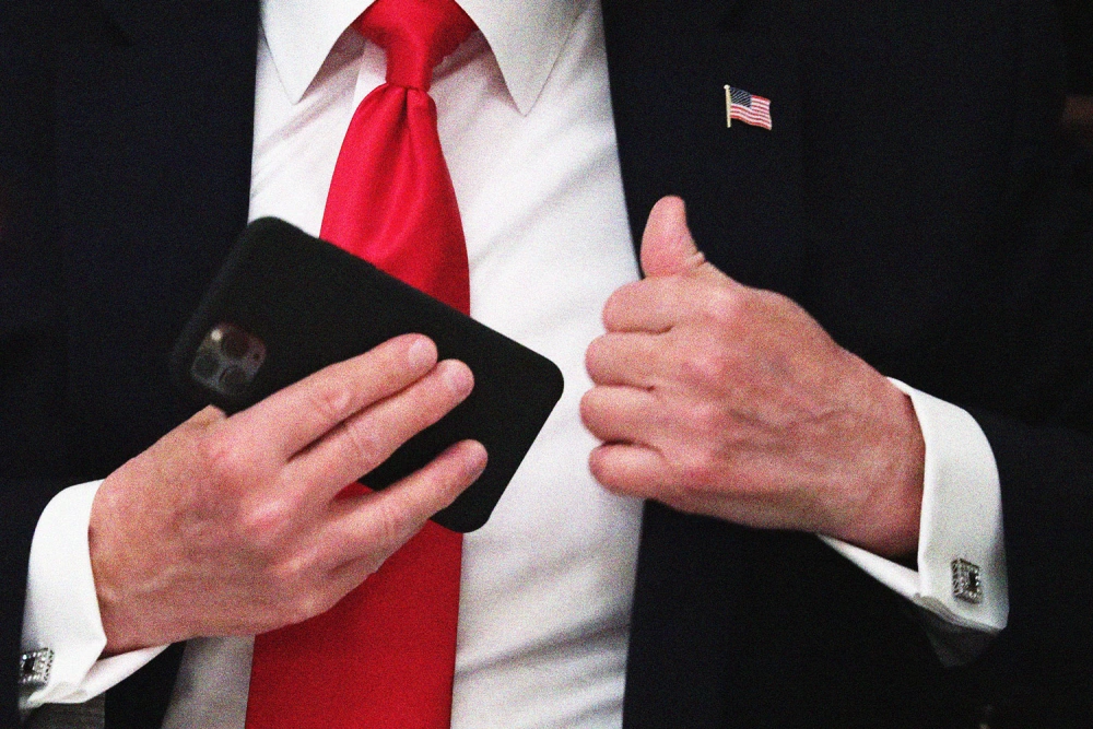 Pic from NBC News of a man's torso in a white shirt, red tie, & a hand holding a cell phone, that resembles Trump.